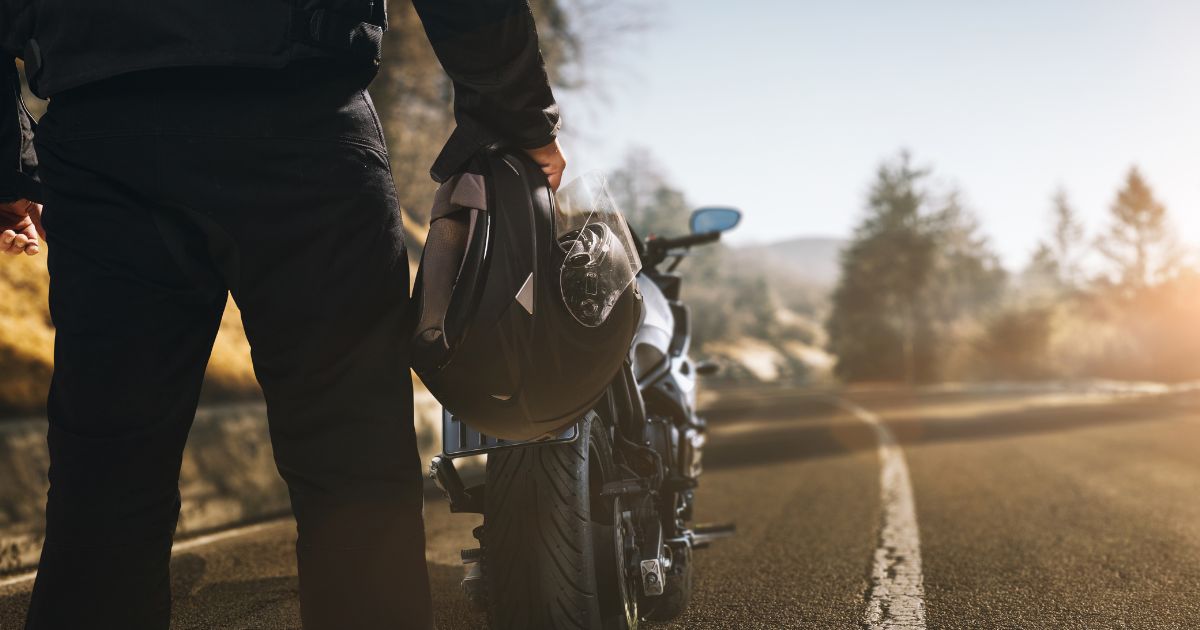 Person standing in front of a motorcycle holding a helmet